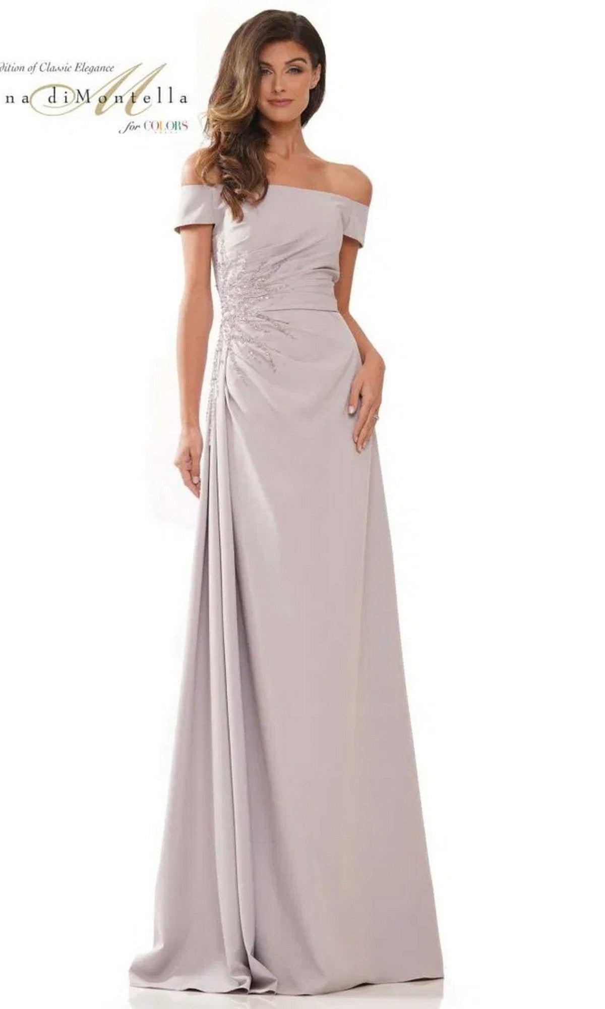 A woman wears the Rina Di Montella RD2806 long formal dress in grey, featuring an off-the-shoulder crepe design, floor-length silhouette, and ruched side detailing, standing against a plain background.